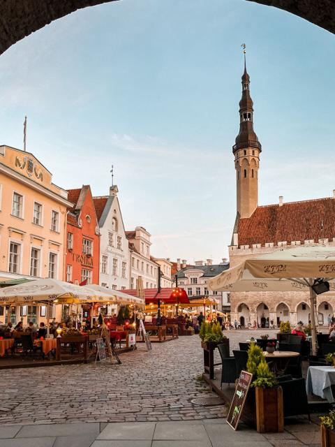 Tallinn Town Hall Square at dusk, seen through a stone archway, with the town hall tower behind