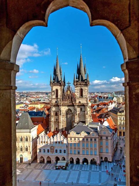 Prague Old Town Square and the spires of the Church of Our Lady before Týn, seen through a stone arch